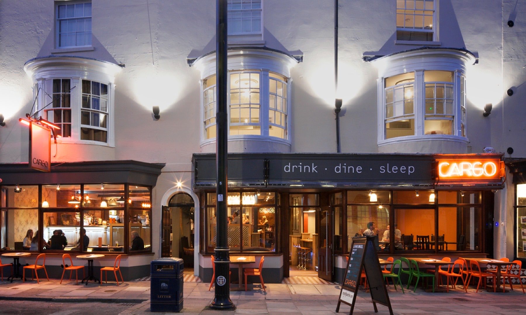 Cargo — drink, dine, sleep — trading at dusk with neon signage